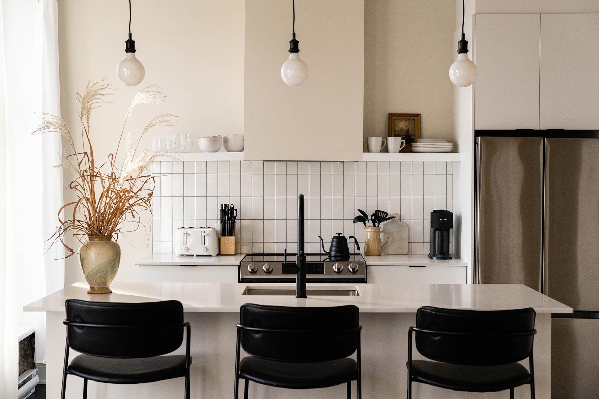 Una cocina moderna con una isla central, sillas negras y una encimera blanca.