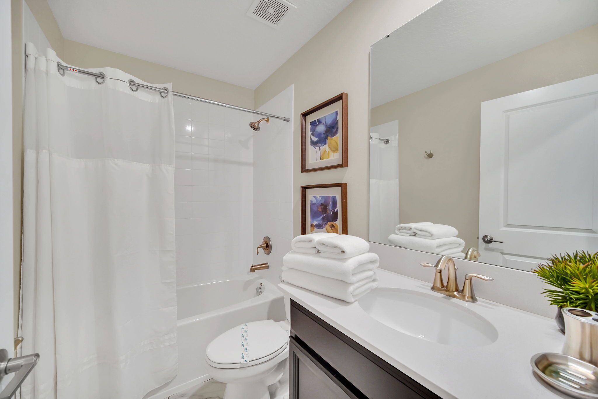 A modern bathroom with a bathtub, toilet, and sink. There are towels stacked on the sink and a framed picture on the wall.