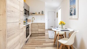 A modern kitchen with wooden cabinets, a white countertop, and a dining area with a table and chairs. - Stylish Apartment in Falmouth, nr Seafront (Falmouth)