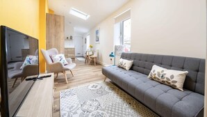 A modern living room with a sofa, armchairs, a TV, and a dining area. - Stylish Apartment in Falmouth, nr Seafront (Falmouth)
