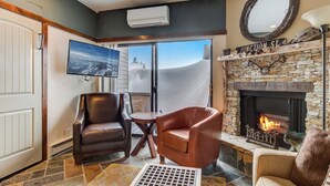 A living room with leather chairs, a fireplace, a television, and a view of the mountains. - Lodge at Mtn Village A104 | Ski-In/Out | Valley View | PCMR | Pool | Hot Tub (Park City)