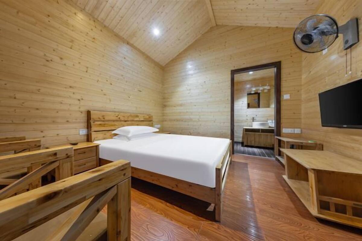 A wooden cabin room with a bed, a TV, a mirror, and a small bathroom.