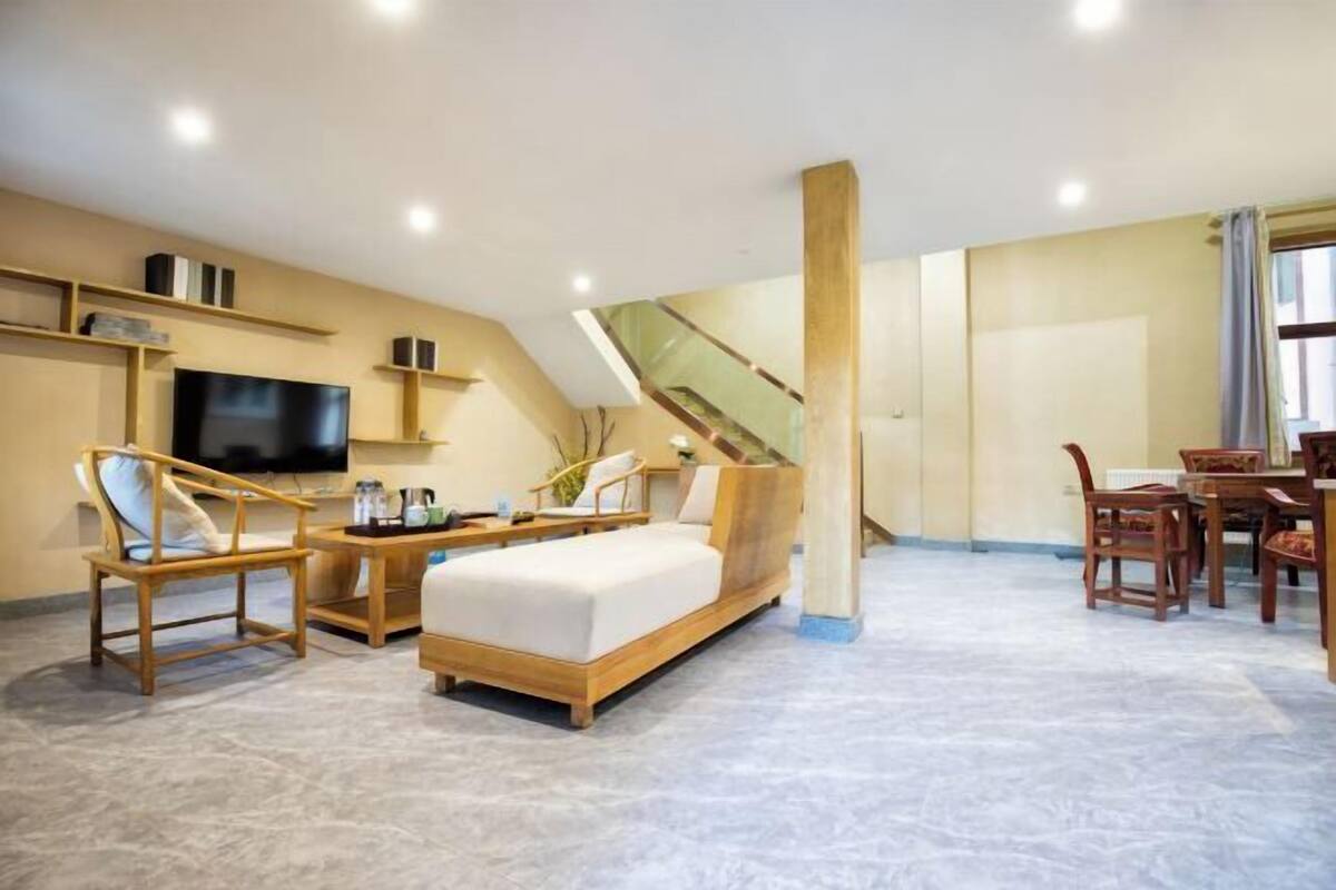 A modern hotel room with a bed, a TV, a dining table, and a staircase.