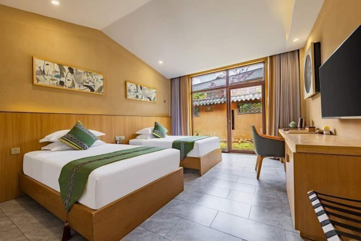 A hotel room with two beds, a desk, a chair, and a large window.