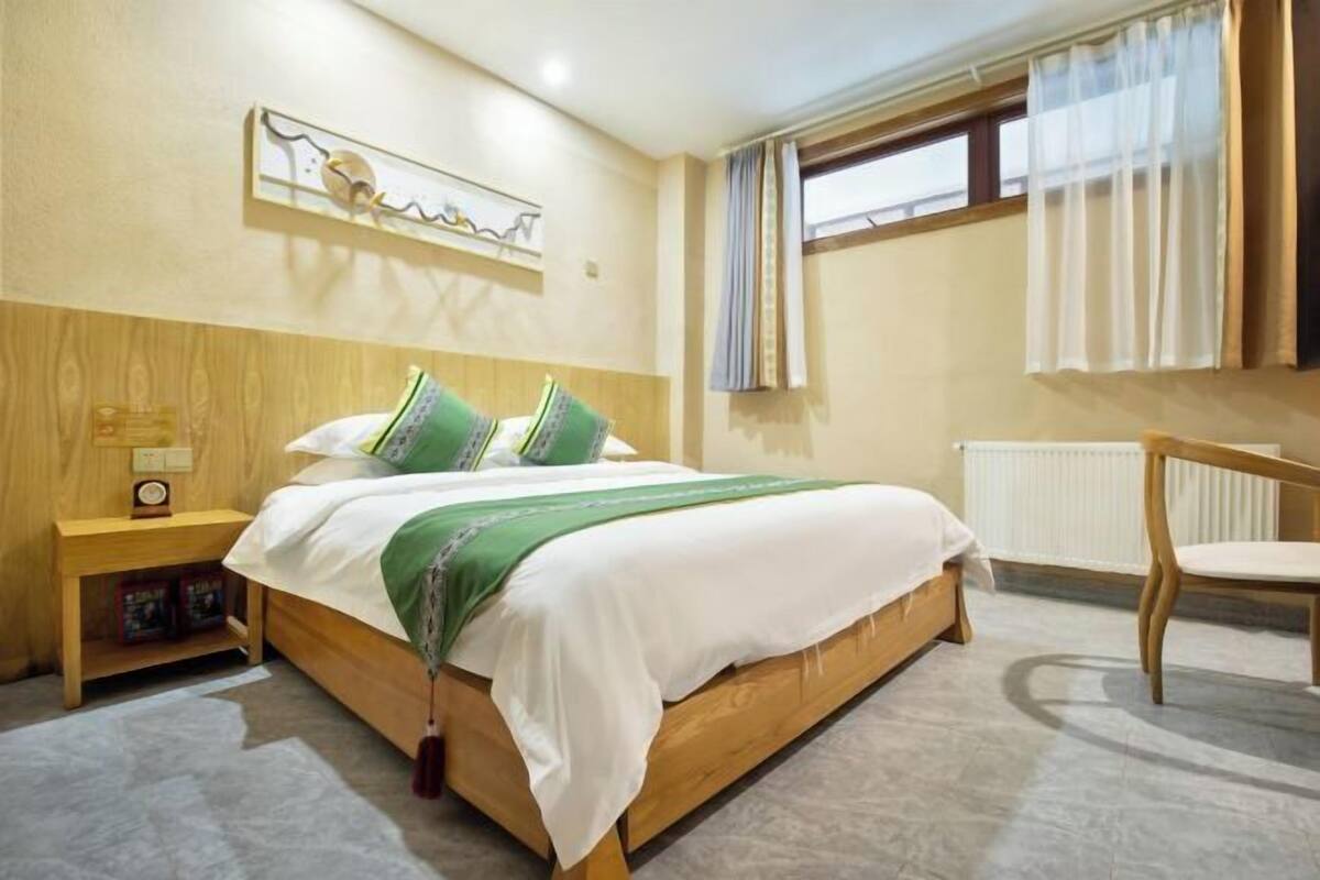 A bedroom with a wooden bed, a nightstand, a chair, and a window with curtains.