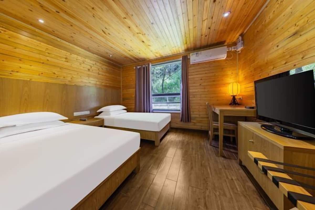 A wooden cabin room with two beds, a TV, and a window with curtains.