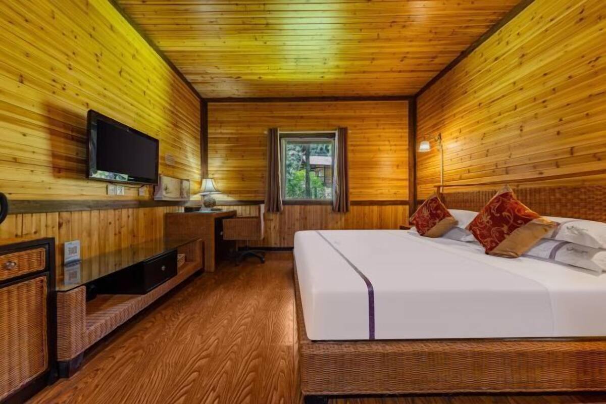 A wooden cabin room with a bed, a desk, a television, and a window.
