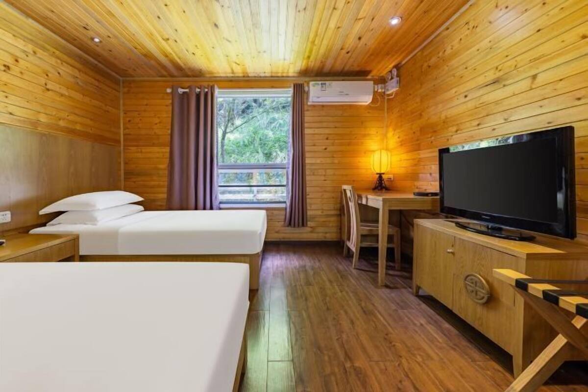 A wooden cabin room with two beds, a TV, and a desk.