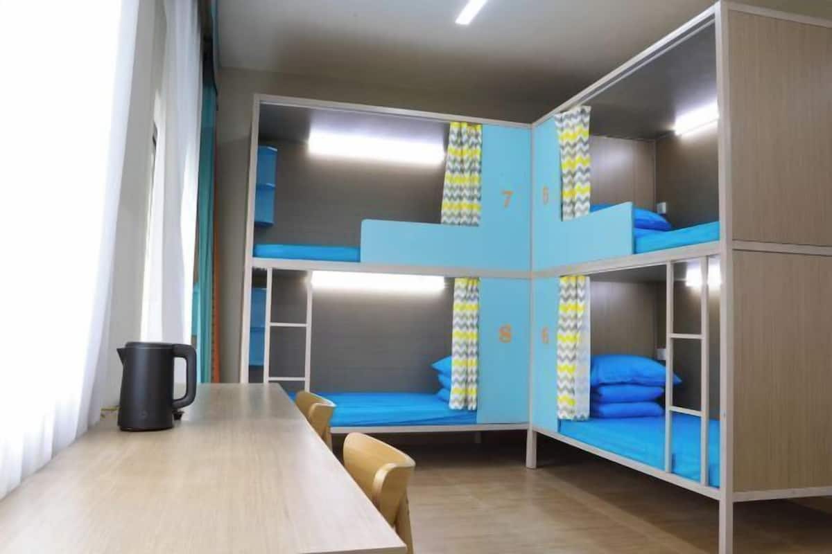 A bunk bed room with a table and chairs, a kettle, and a window with curtains.
