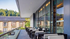 A modern outdoor seating area with tables and chairs, overlooking a residential neighborhood and a forested hill. - Xianfeng Pingbaying Forest Hotel (Xianfeng)