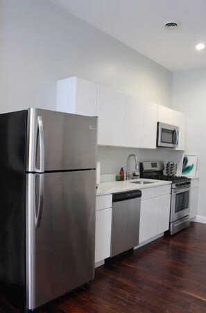 A modern kitchen with stainless steel appliances, white cabinetry, and a wooden floor.