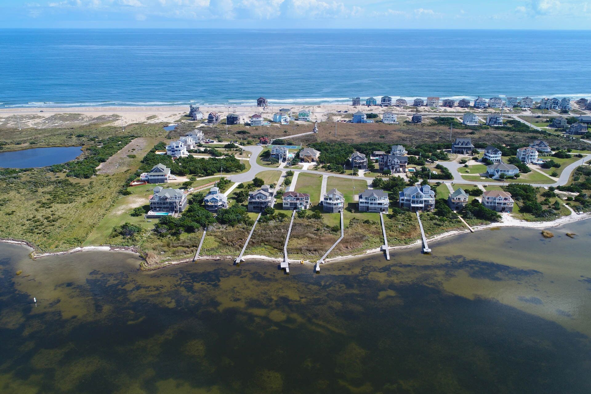 An aerial view of a coastal residential area with houses, a beach, and a water body.