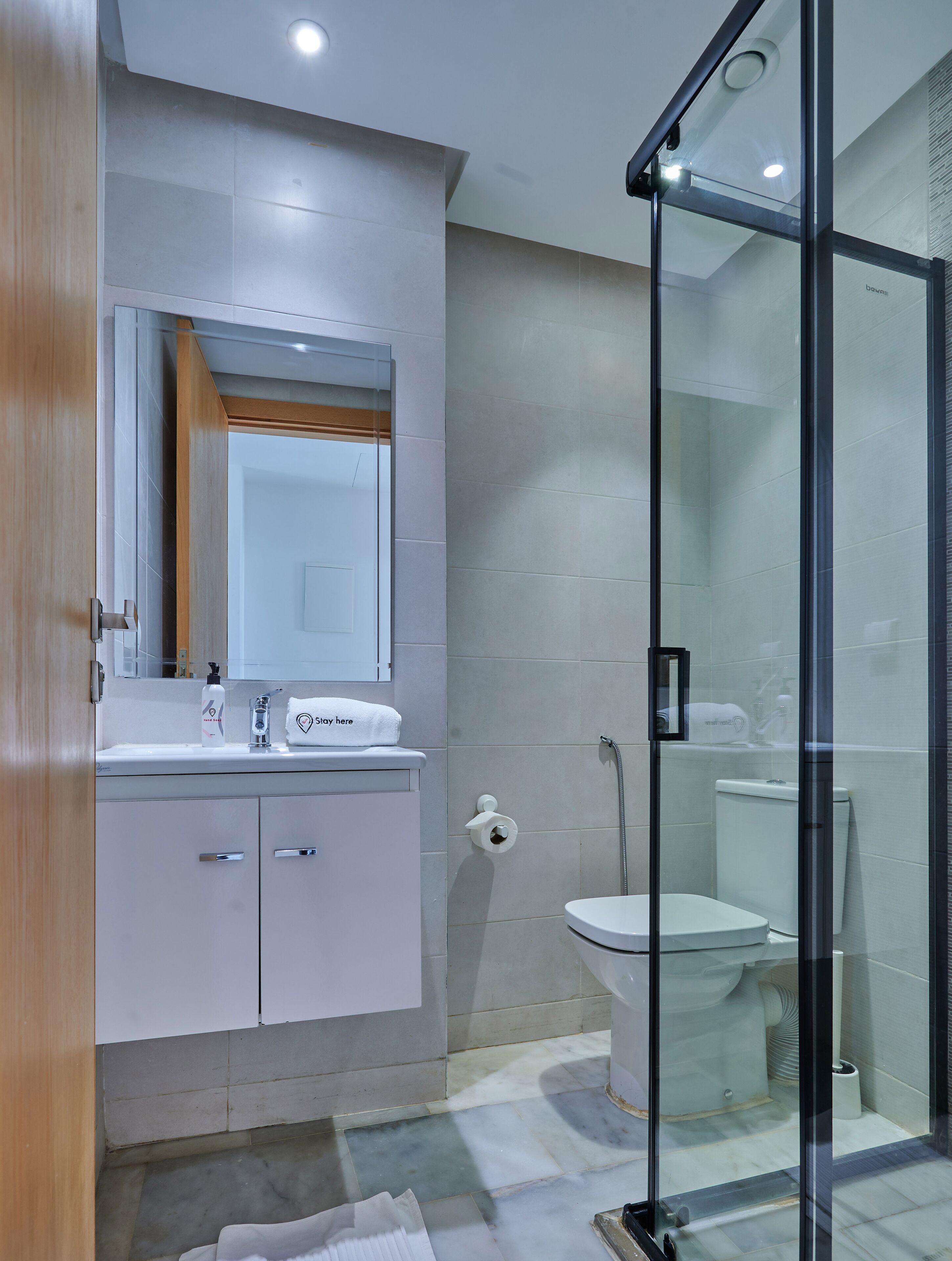 A modern bathroom with a glass shower enclosure, a white sink with a mirror above, and a toilet.