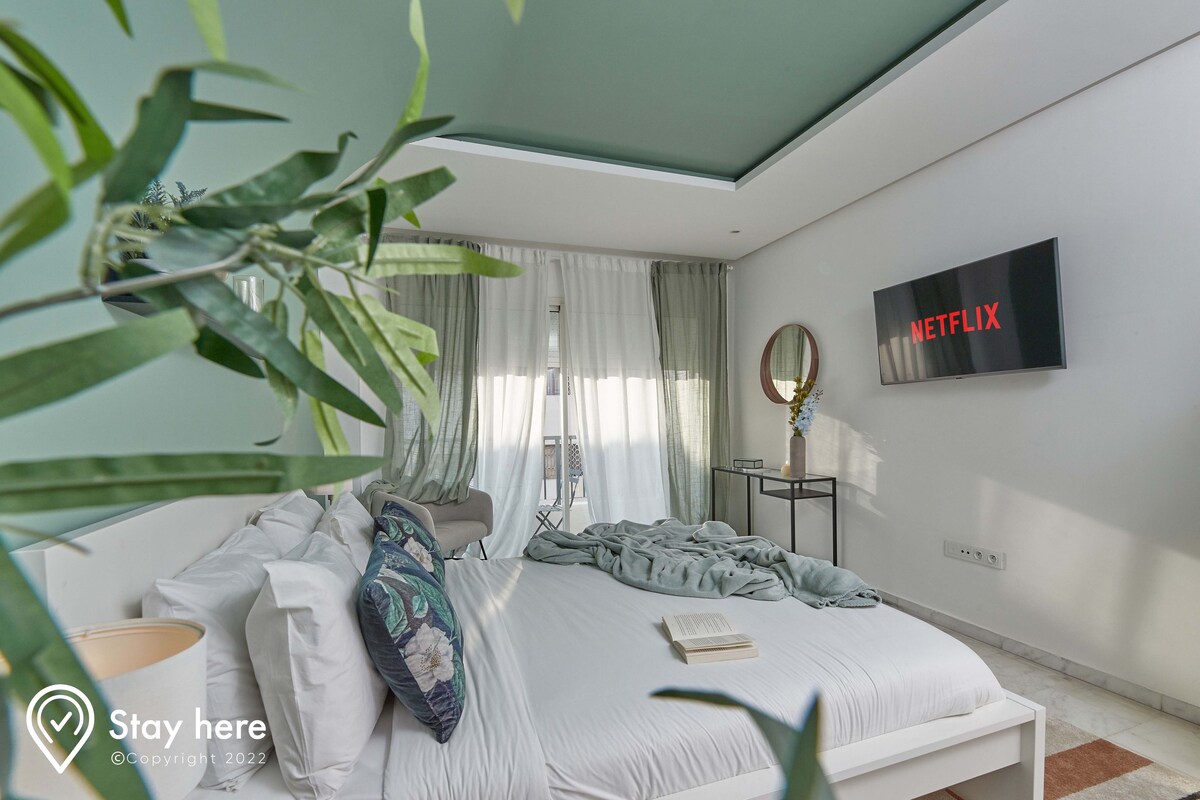 Un dormitorio moderno con una cama, una mesita de noche, un espejo y un televisor de pared que muestra "NETFLIX".