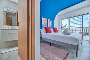 Un dormitorio moderno con una cama grande, un baño con espejo y artículos de aseo, y un balcón con vistas.