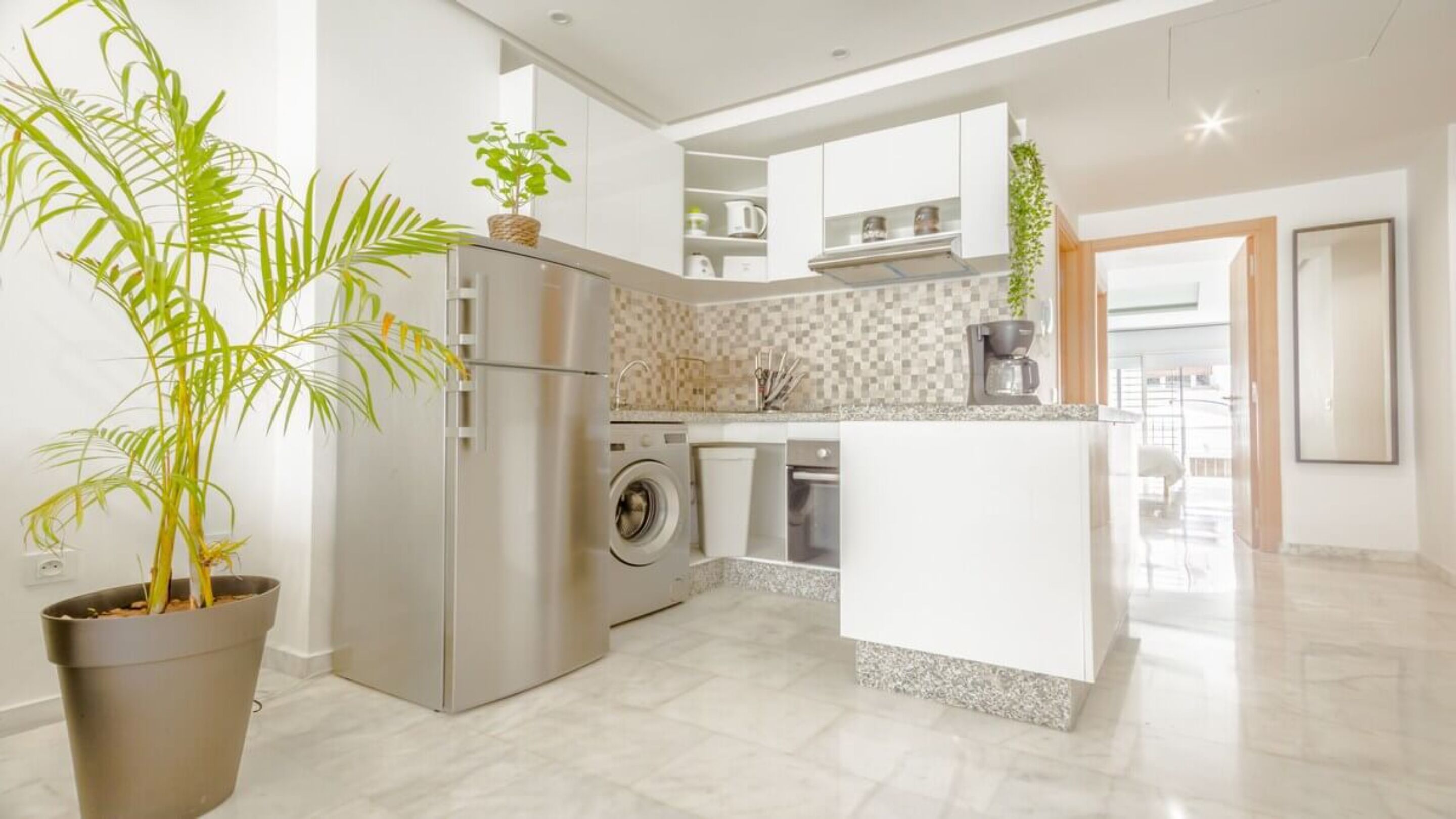A modern kitchen with a central island, built-in appliances, and a potted plant.