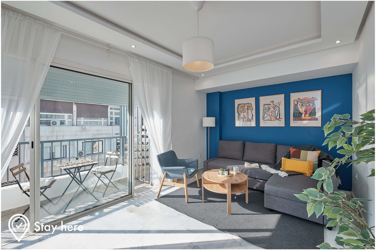 A modern living room with a grey sofa, a wooden coffee table, and a blue accent wall with artwork.