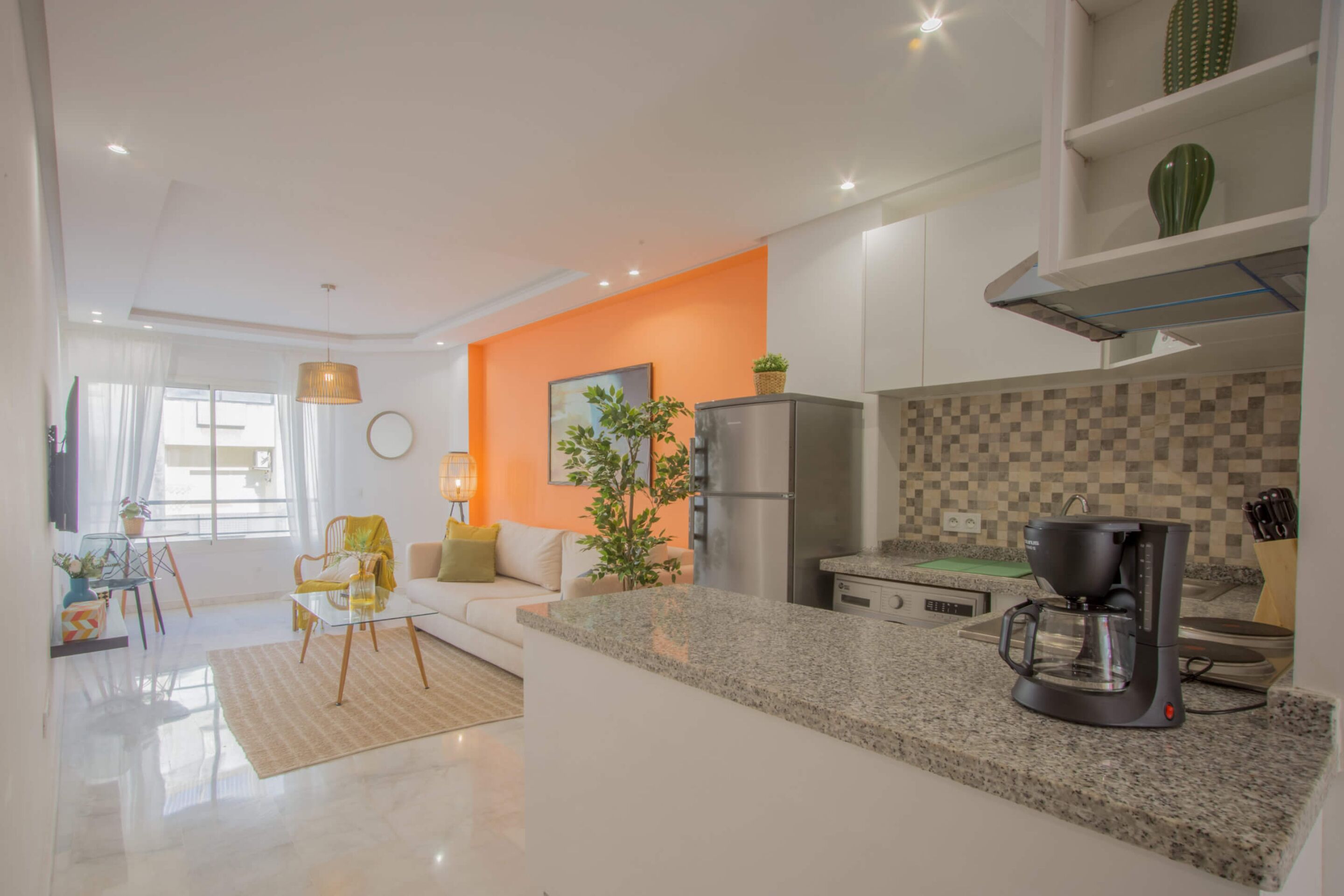 A modern kitchen with a granite countertop, a coffee maker, and a refrigerator.