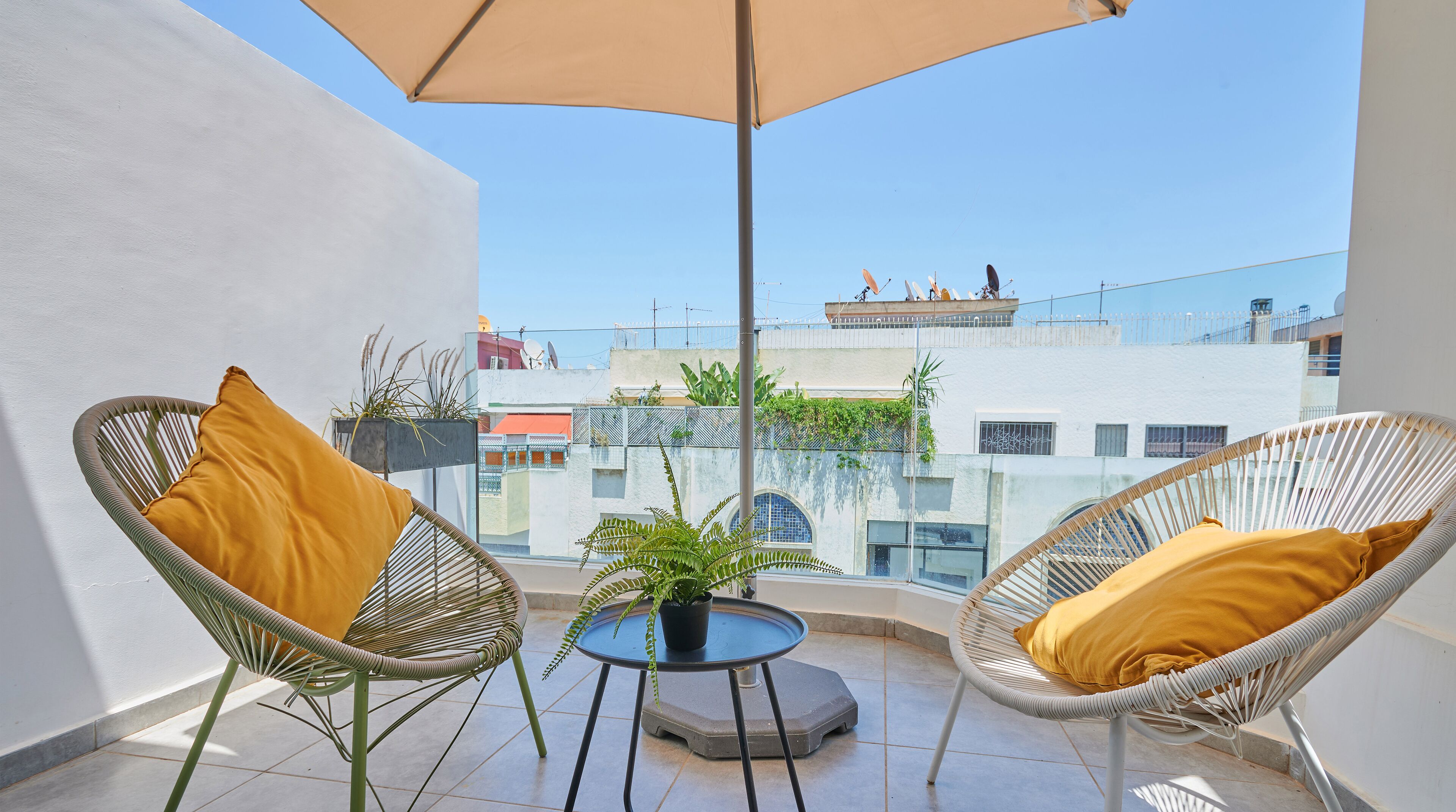 A balcony with two wicker chairs, a small table, and a potted plant.