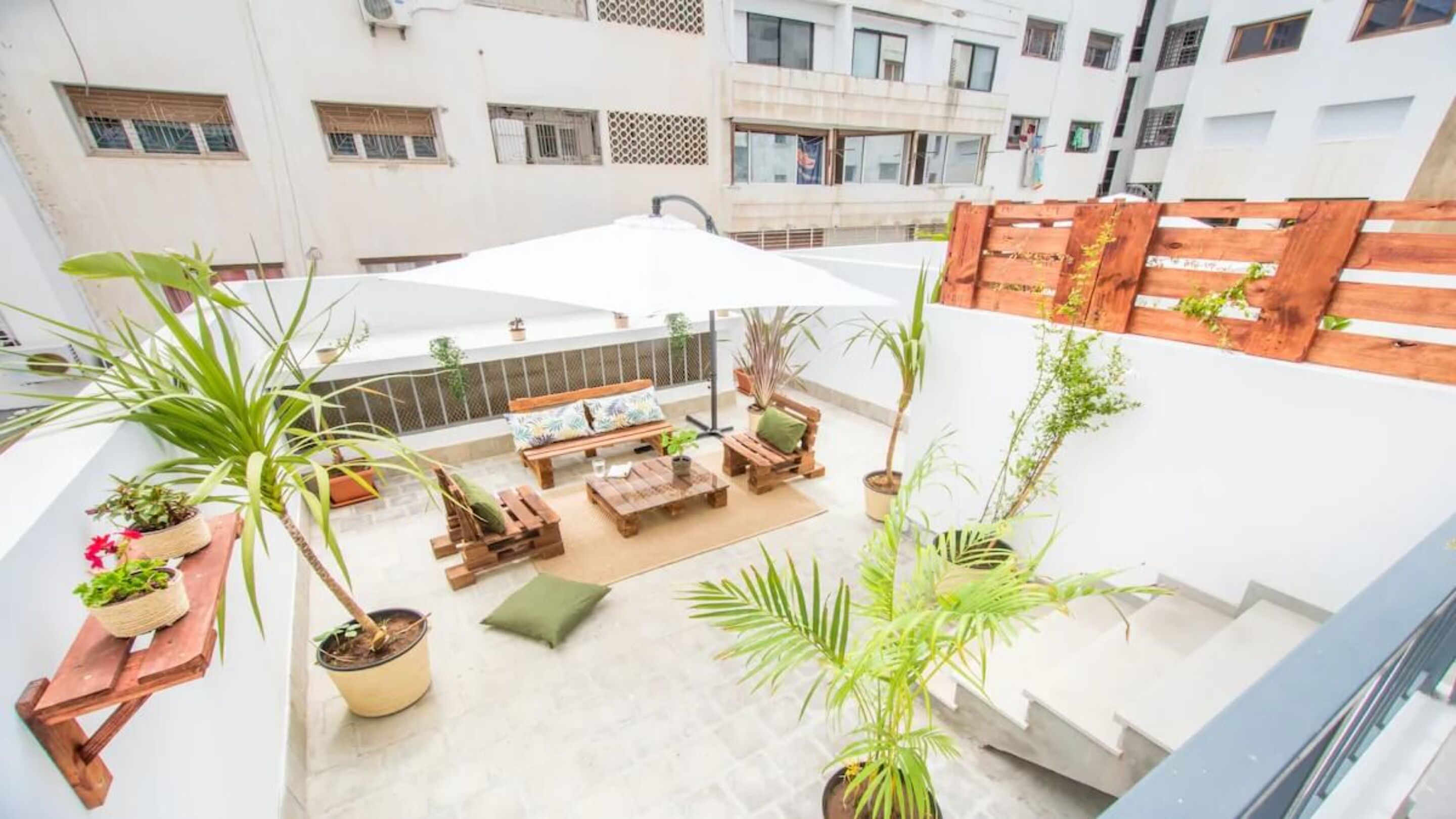 An outdoor patio with wooden furniture, potted plants, and a white umbrella.