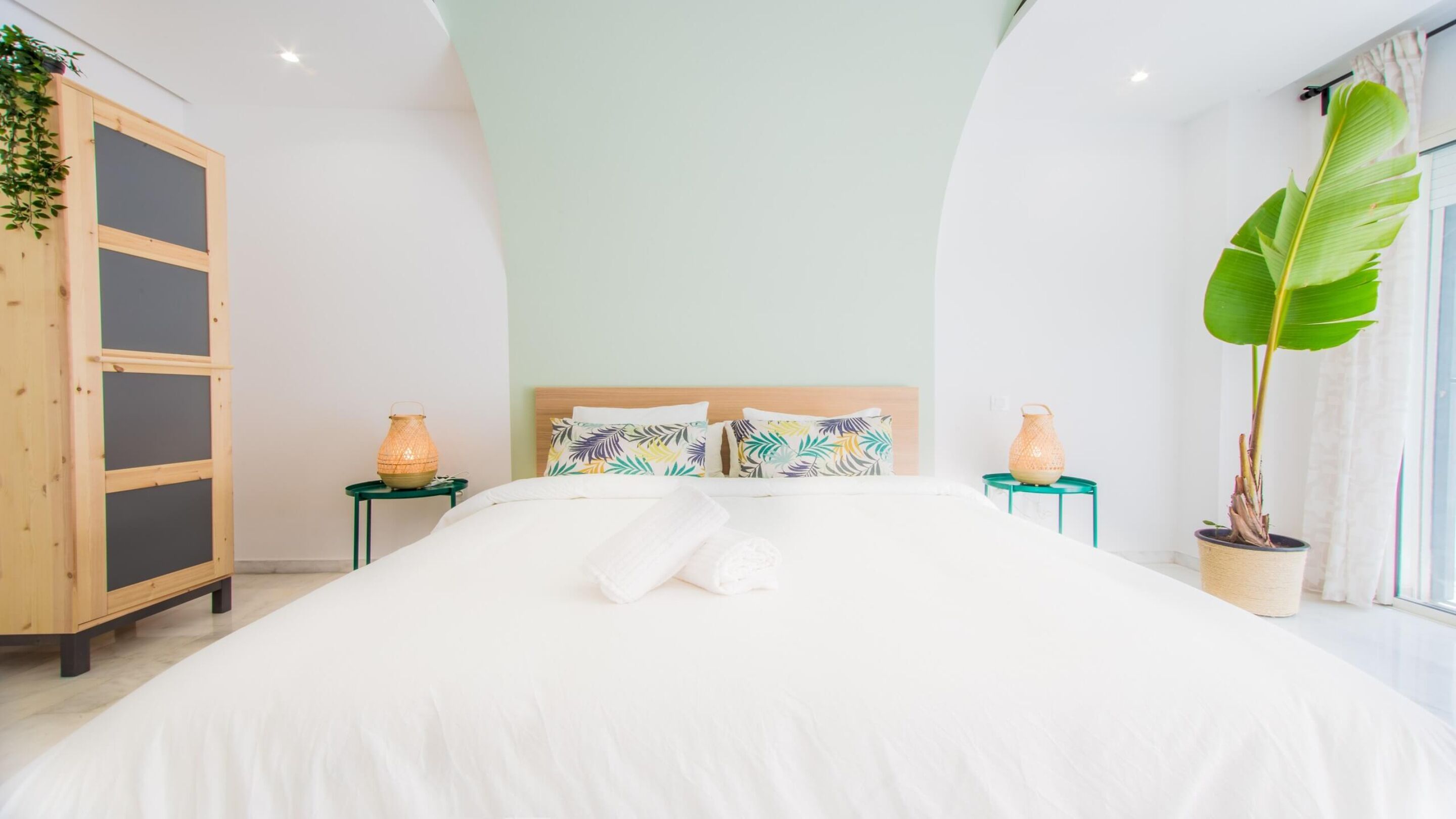 Un dormitorio moderno con una cama grande, dos mesitas de noche, un armario de madera y un amplio ventanal con vistas.