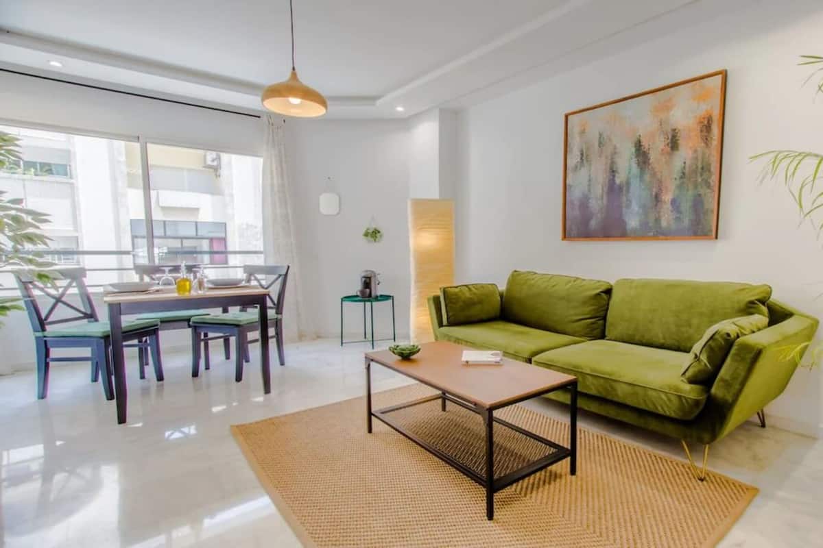 A modern living room with a green sofa, a coffee table, and a dining area with a table and chairs.