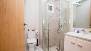 Un baño moderno con ducha de vidrio, inodoro y tocador con espejo.
