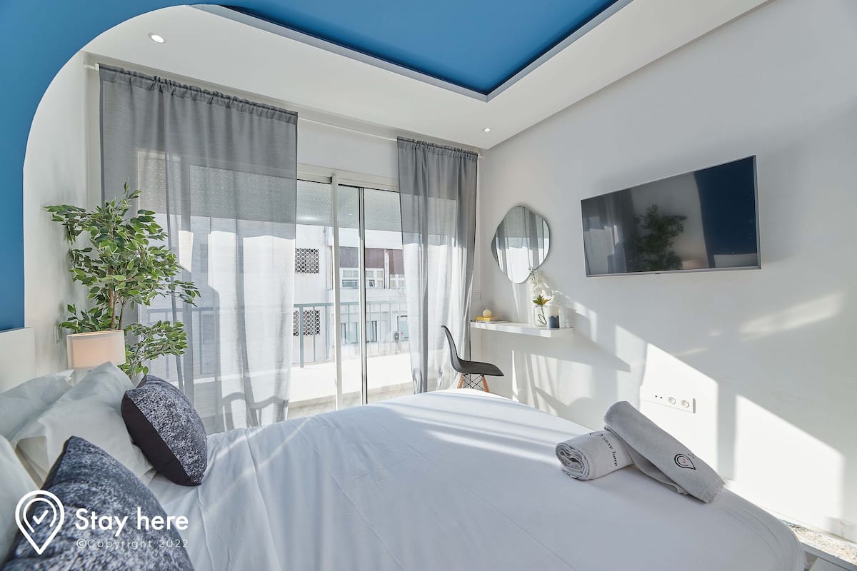 A modern bedroom with a bed, a potted plant, a chair, a desk, and a TV.
