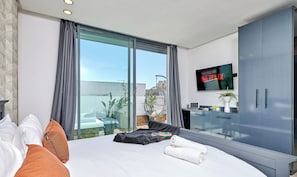 A modern hotel room with a large bed, a desk, a TV displaying 'NETFLIX', and a balcony with a view.