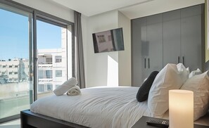 A modern hotel room with a large bed, a TV mounted on the wall, and a view of the city through large windows. - StayHere Rabat - Agdal Collection (Rabat)