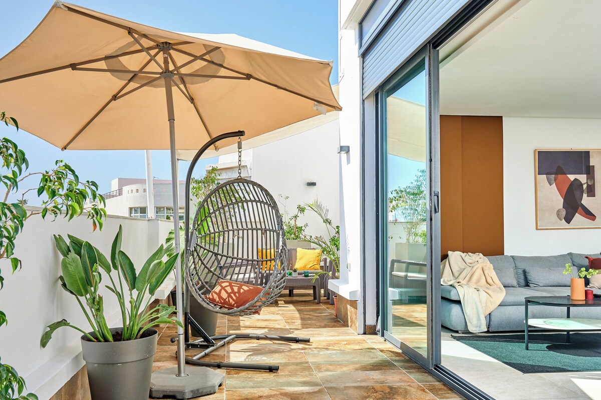 A modern outdoor patio with a swing chair, a large umbrella, and potted plants.