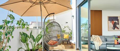 A modern outdoor patio with a swing chair, a large umbrella, and potted plants.