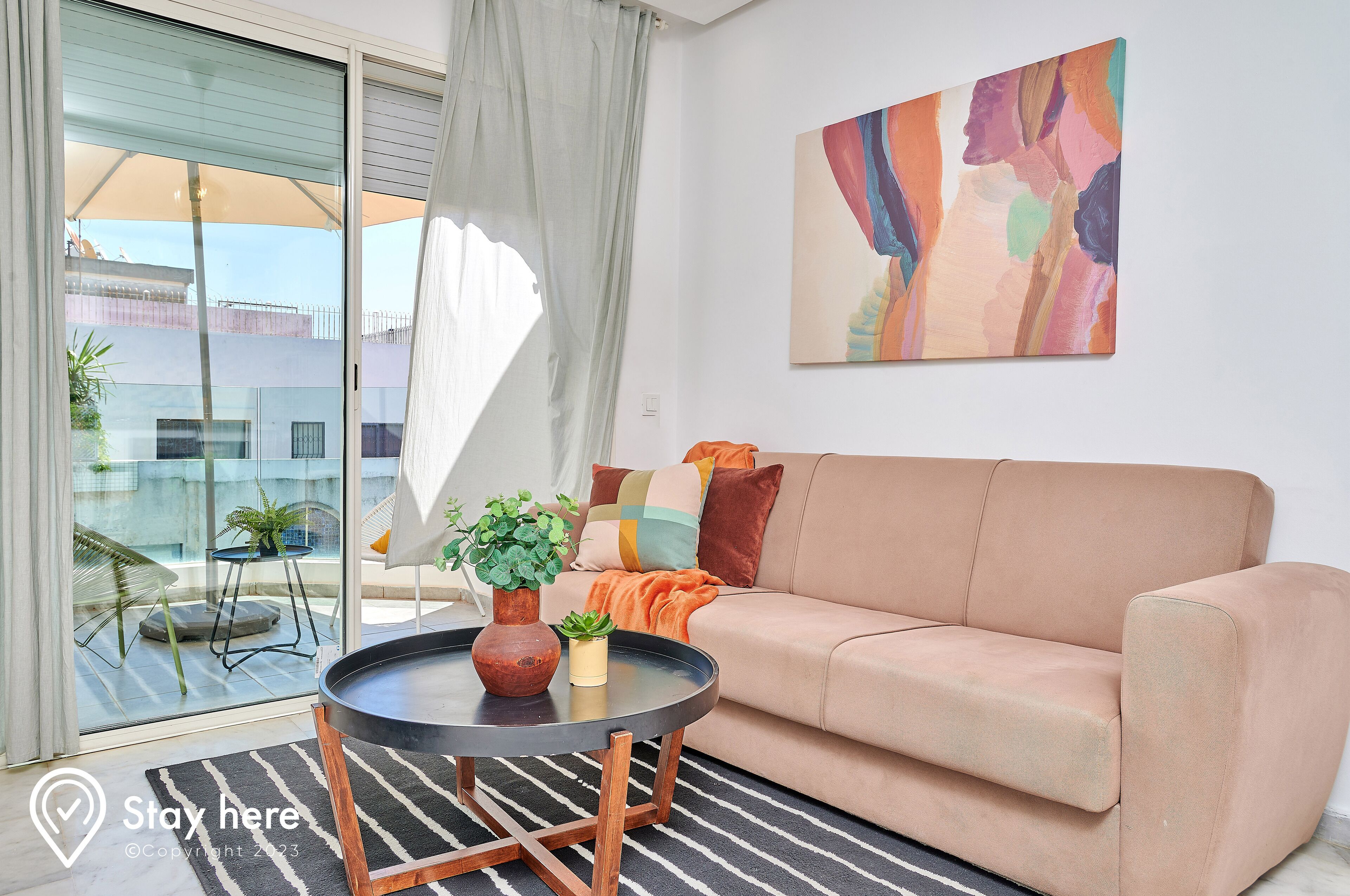 A living room with a beige sofa, a round black coffee table, and a painting on the wall.