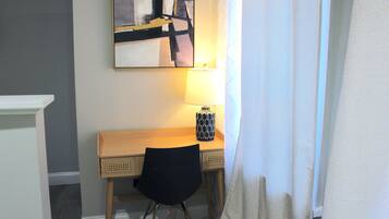 A hotel room with a wooden desk, a black chair, a lamp, and a painting on the wall.