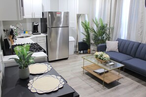 Une cuisine moderne équipée d’un réfrigérateur en acier inoxydable, d’une cuisinière à gaz et d’une machine à café. On y trouve une table à manger avec des sets de table, ainsi qu’une table basse en verre dans l’espace salon.