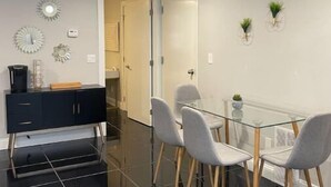 Uma sala de jantar moderna com mesa de vidro e cadeiras cinzentas, um armário preto e arte decorativa na parede.