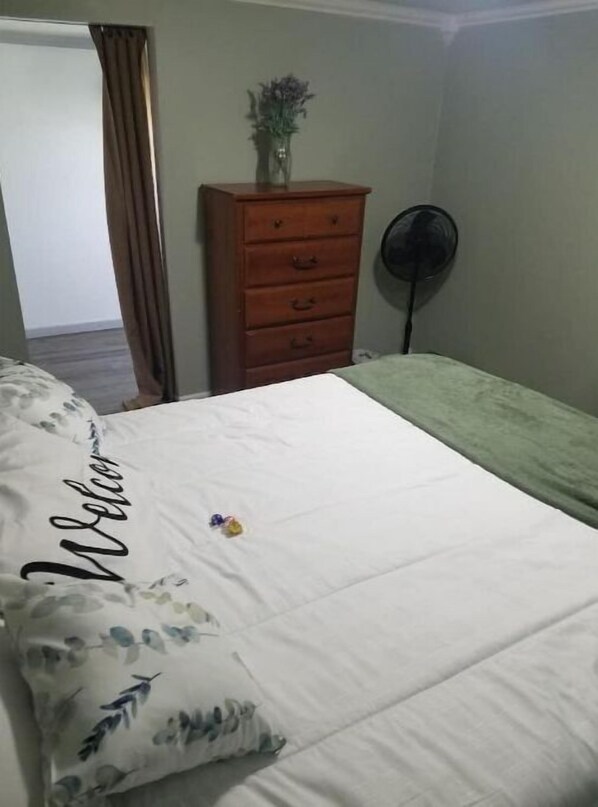 Une chambre à coucher avec un lit, une commode, un ventilateur et une porte.