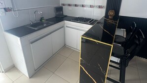 A compact kitchen with white cabinets, a black countertop, and a small dining area with a black table and chairs. - Aloha Beach Sai (San Andrés)
