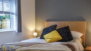 Un lit bien fait, avec une tête de lit en bois, une lampe de chevet et une fenêtre avec des rideaux.