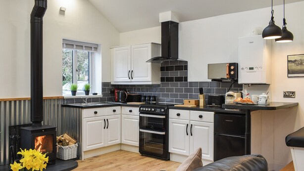 Une cuisine moderne avec des meubles blancs, une cuisinière noire et une hotte noire. On y trouve un coin repas avec un canapé en cuir noir et un vase rempli de fleurs jaunes.
