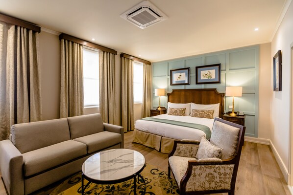 Una habitación de hotel con una cama, un sofá, una silla, una mesita y dos lámparas de noche.