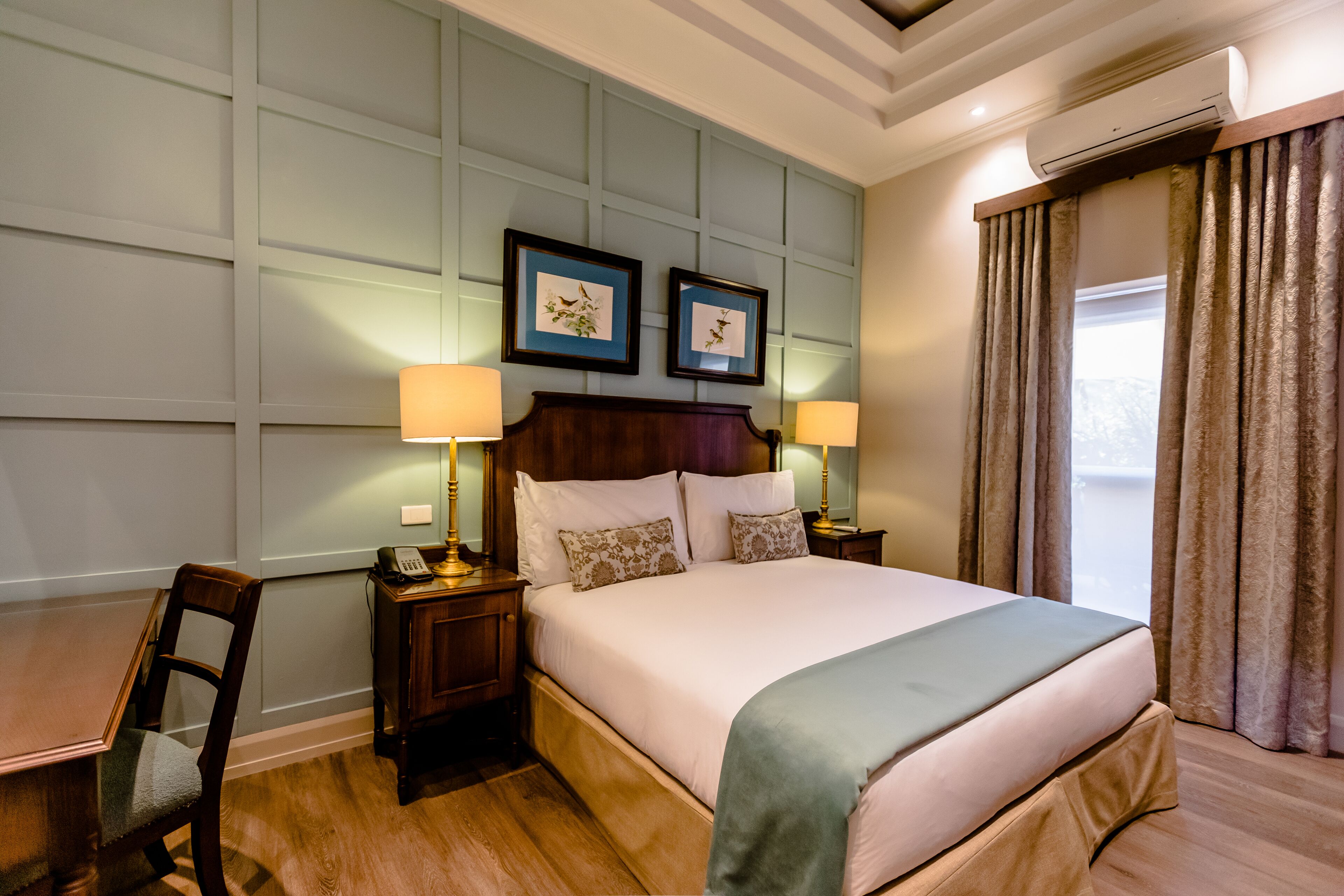 A hotel room with a large bed, two bedside tables with lamps, a wooden chair, and a wall-mounted air conditioner.