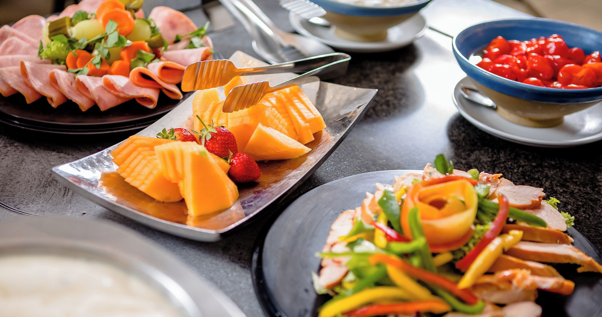 A buffet with various food items including sliced meats, fruits, and vegetables.