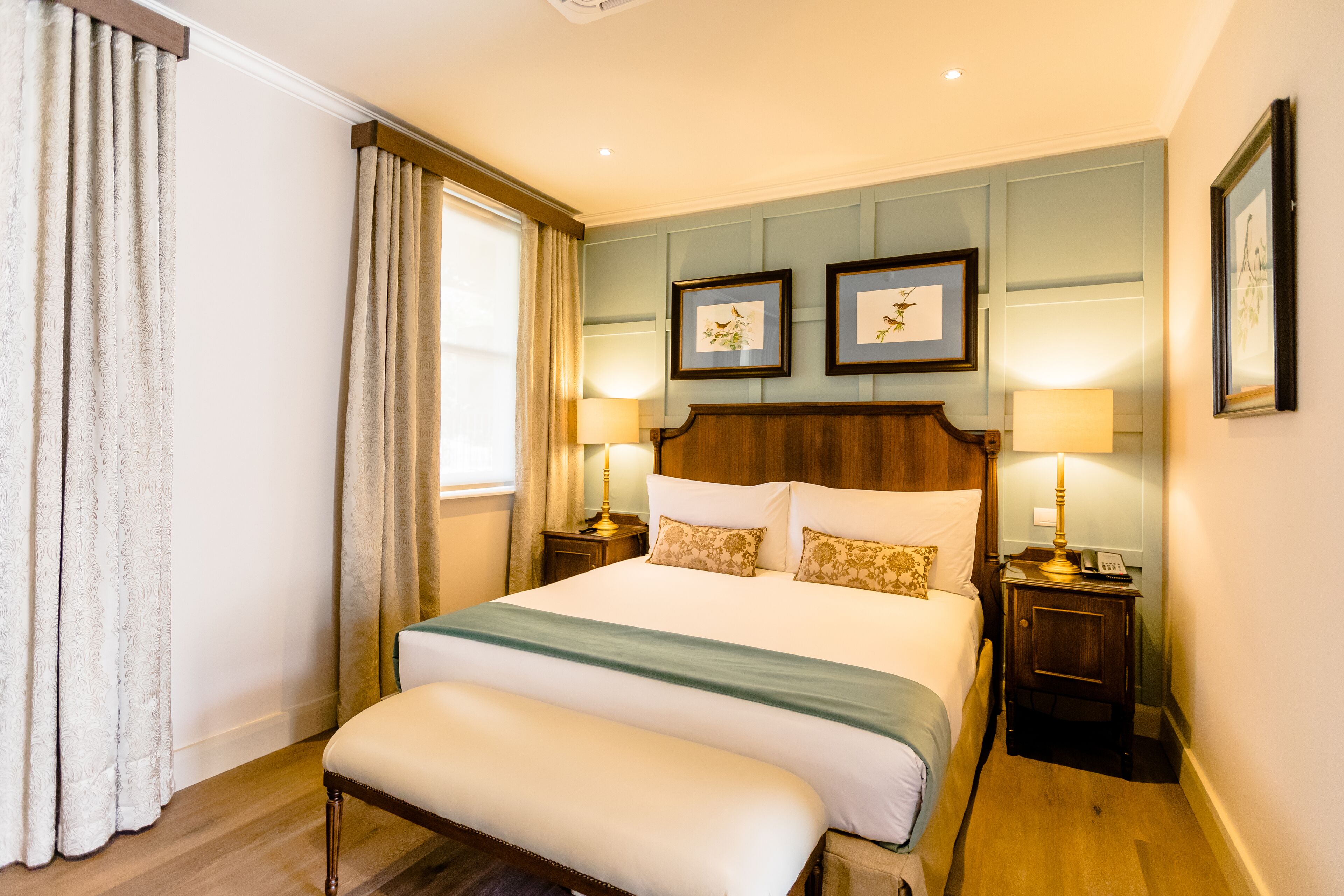 Habitación de hotel con una cama grande, dos mesitas de noche, un banco y cuadros en la pared.