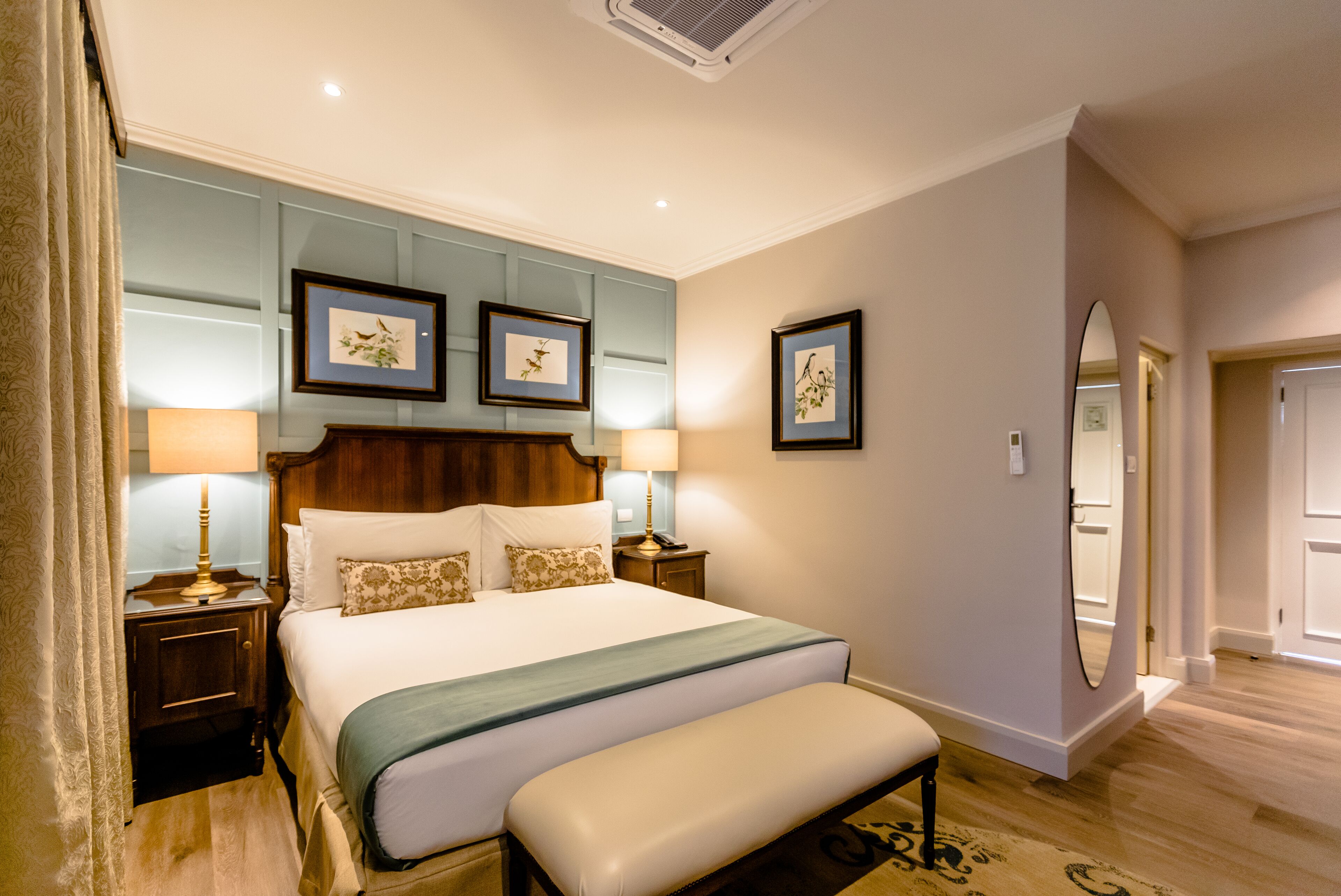 A hotel room with a large bed, bedside tables, a bench, and framed pictures on the wall.
