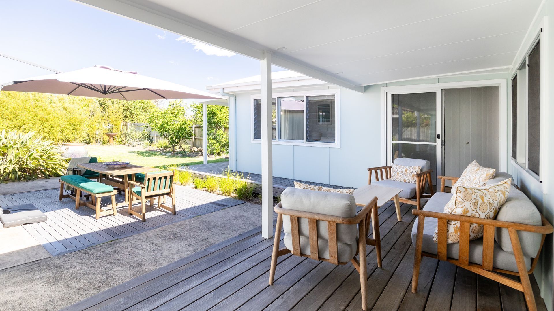 Eine überdachte Terrasse im Freien mit Holzmöbeln, einem Tisch und einem großen Sonnenschirm.