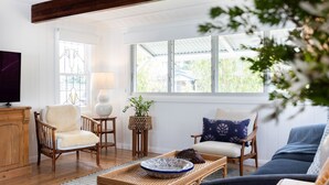 A cozy living room with wooden furniture, a television, and a large window with a view of greenery.