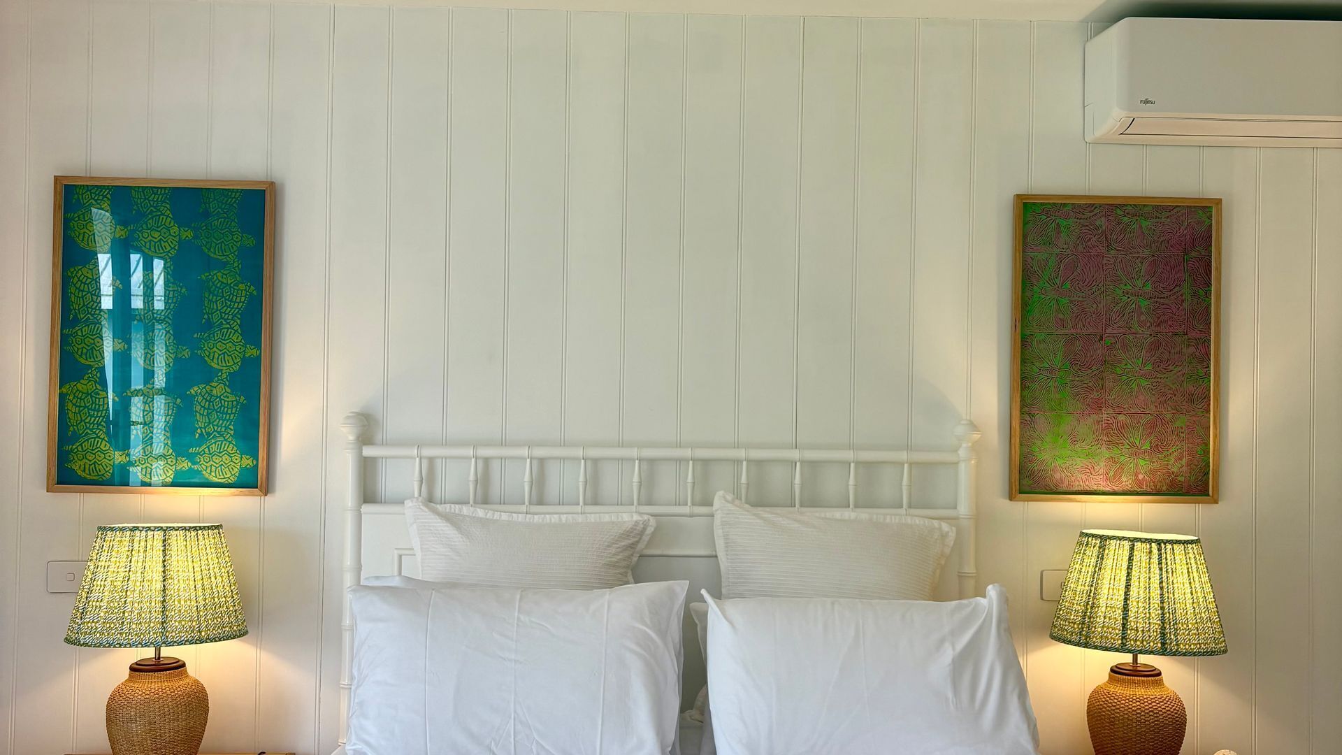 Ein Bett mit weißer Bettwäsche, zwei Lampen an beiden Seiten und zwei gerahmte Kunstwerke an der Wand.