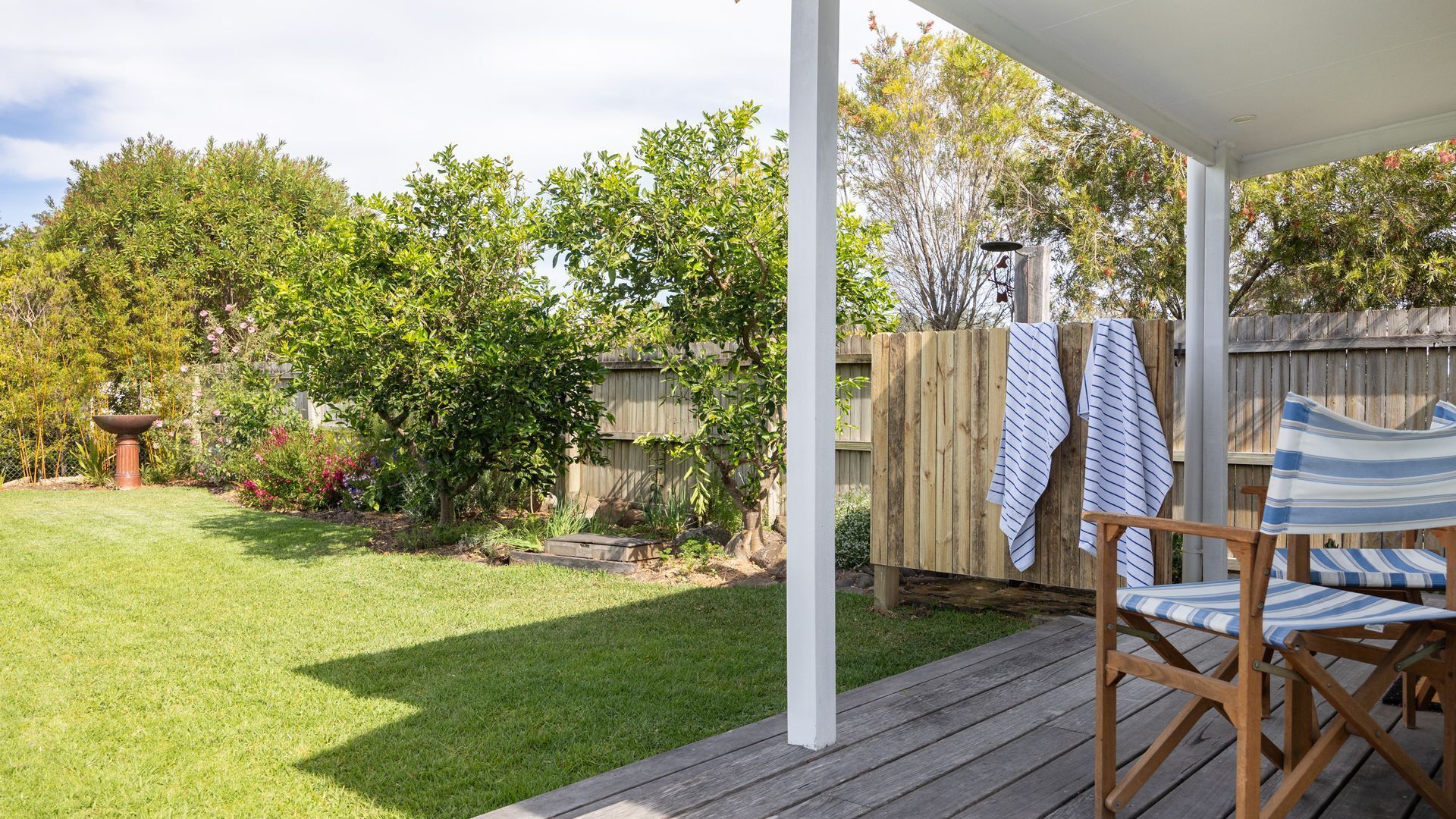 Une terrasse couverte avec une plateforme en bois, une chaise et un fil à linge suspendu où sont étendues des serviettes.