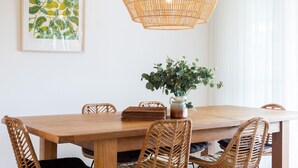 A wooden dining table with wicker chairs, a woven pendant light, and a potted plant.